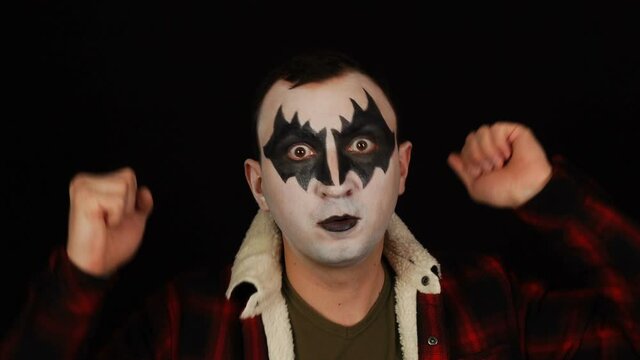 Man in demon makeup dancing with raised hands on black background