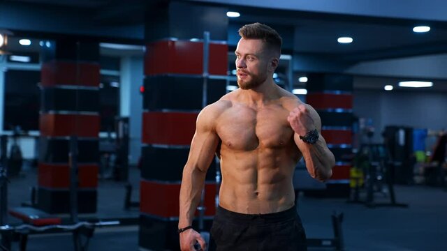 Muscle athlete strongman pumps muscules in a gym after heavy training. Perfect torso with strong abs. Handsome power male with naked torso.