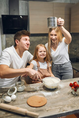 A full multicultural family with an adorable daughter gathered in a modern kitchen, preparing pancakes together. Making cake mix, pouring milk, socializing pleasure and culinary hobby