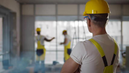 Back view of foreman in yellow hardhat watching crew doing renovation