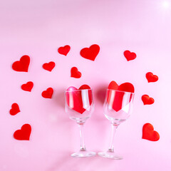 Happy Valentine's Day greetings. Two wine glasses with red hearts on a pink background decorated with red heart shapes, flat lay, top view. Symbol of love, date, engagement