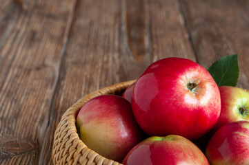 Ripe red organic apples in a wicker basket on a rustic wooden table.