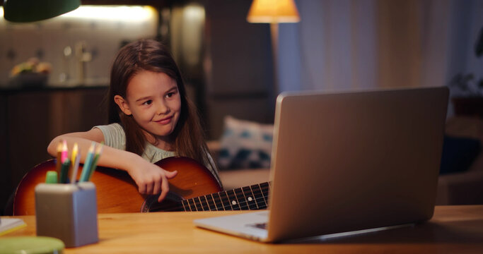 Happy Little Child Learning To Play Guitar While Watching Lessons At Laptop And Smiling At Home