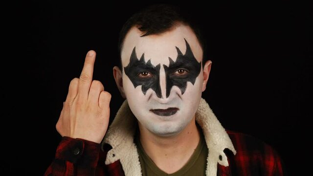 Man in demon makeup making a fuck gesture on black background