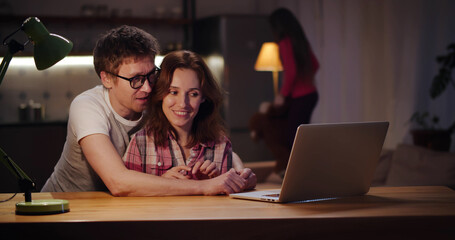 Happy couple surfing internet on laptop with little daughter playing on background