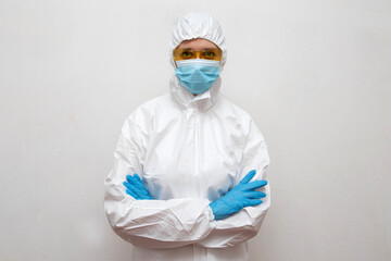 Woman doctor in protective suit, medical mask and yellow glasses with arms crossed in studio with white background