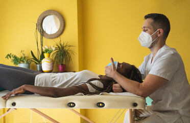 Physiotherapist wearing a mask applying pressure to the neck of a patient