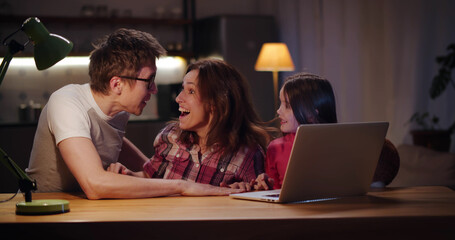 Excited mom, dad and daughter triumph and win game on laptop