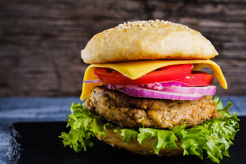 Fresh delicious homemade veggie burger lies on natural slate on rustic wooden background. Delicious tasty burger with lettuce, cheese, onion and tomato. buckwheat and lentil cutlet