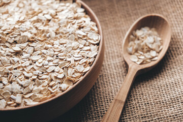 Dry oatmeal in a wooden bowl and spoon on a linen fabric background. Copy, empty space for text