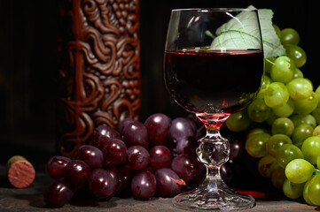 Red wine in glass with vintage bottle and with bunch of red and white grapes on wooden background.
