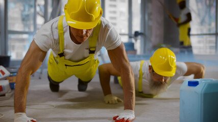 Mature builders in uniform doing pushups during break at work site