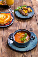 A cup of soup, seasoned with herbs, fresh pastries and fried potatoes with cutlets on a brown wooden background.