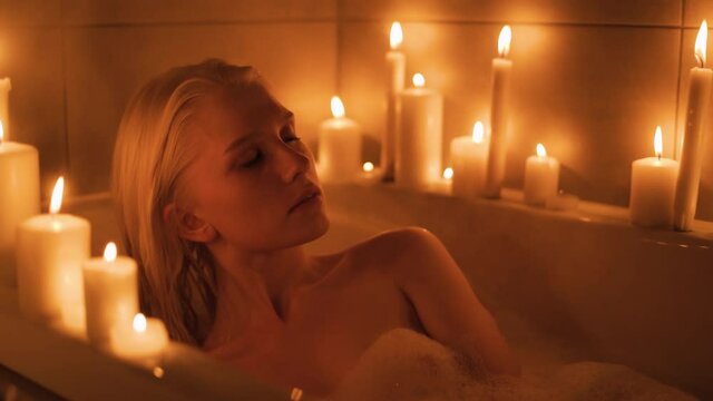 Slow motion shot of a young woman having a bath in the light of candles. slow motion