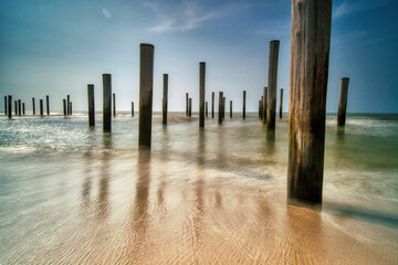 Long exposure seascape. Taken at the North Sea in Petten with the pole village in the sea, Blue sky, sun and shodows