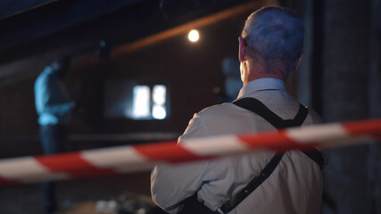 Back view of detective watching forensic specialists examining dead body at crime scene
