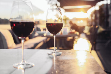 Two glasses of red wine on a sunny fancy restaurant terrace. Marble tables, cosy couch, sunset light, rooftop 