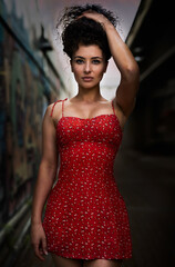 Fototapeta premium A beautiful young curly-hair woman in a little red dress is walking on the street. - Portrait Photography. 