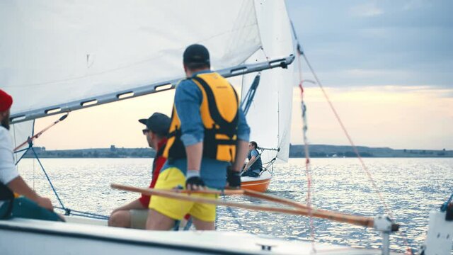 Close up motion camera side view of yacht going across large lake, wide river, sea or ocean. Sailors men wearing protective life vests, drive the yacht, enjoy marine voyage. Active water lifestyle