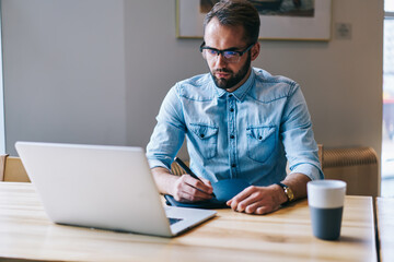 Focused man looking at laptop taking notes