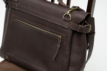 Details of brown men's shoulder leather bag for a documents and laptop on a brown chair with a...