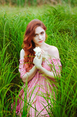 Outdoor portrait of young redhead woman in field of green grass with pink peony. Woman's Day. Female spring, summer fashion concept.