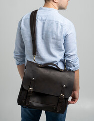 Brown men's shoulder leather bag for a documents and laptop on the shoulders of a man in a blue shirt and jeans with a white background. Satchel, mens leather handmade briefcase.