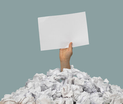 Hand schaut aus Papierhaufen und h&auml;lt Schild in die Luft