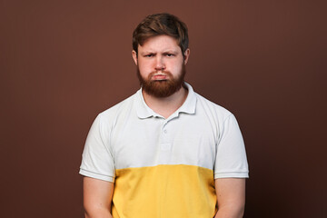 Millennial guy is upset, disappointed or offended by pursed lips posing against a brown studio...