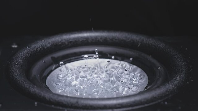 Dark Wave Audio and Black Water Liquid on a Plate. Subwoofer speaker with water. Droplets explode over the sound of the bass. Liquid jumps on the audio speaker. Background for a party. Slow motion.