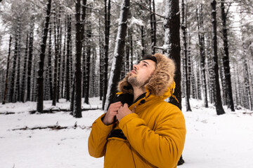 Fototapeta na wymiar Young man with a yellow anowak posing at the middle of a snowy forest