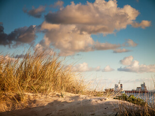 sand dune with sea grass and clouds with ship in the background