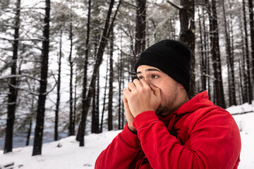 Young man trying to warm his hands on a snowy forest