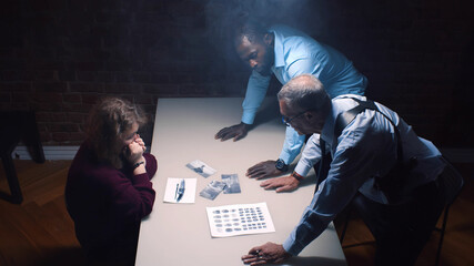 Two police officers and woman criminal in interrogation room - obrazy, fototapety, plakaty