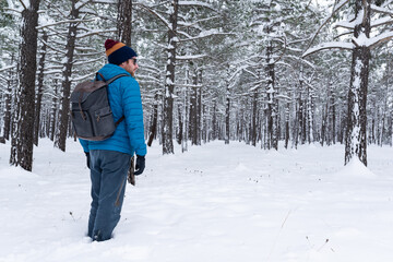 Fototapeta na wymiar Side view of a young man practising trekking on a beautiful snowy forest. 