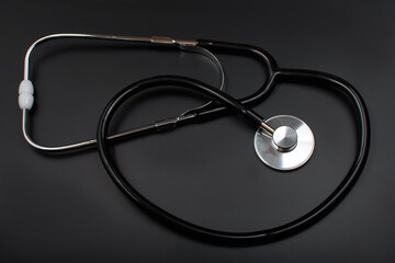 Stethoscope with black rubber tube, over black background. Medical instrument for therapist and cardiologist. A device for listening to heart and pulse