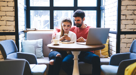 Young couple spending time in restaurant while watching photos on smartphone