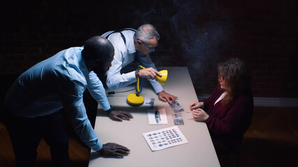 Policemen interviewing suspect woman with lamp glowing into her face