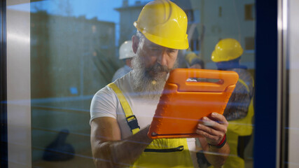 Senior foreman inside house being renovated using digital tablet standing near window
