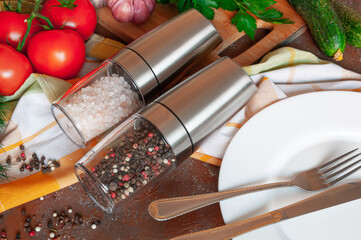 Electric spice mills. With Himalayan salt and pepper. Lie on the table. Nearby are cutlery and vegetables.