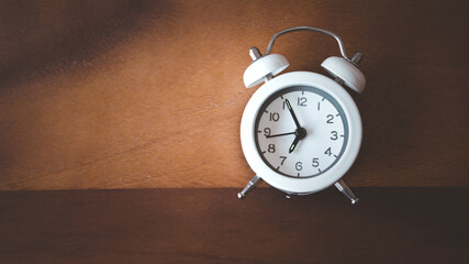 Naklejka premium white alarm analog clock on dark brown wood background, time passing concept , deadline , reminder, schedule and planning