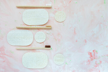 Round and oval luffa discs and natural wooden bamboo toothbrushes. Plastic free and zero waste concept. Top view, copy space, pink background