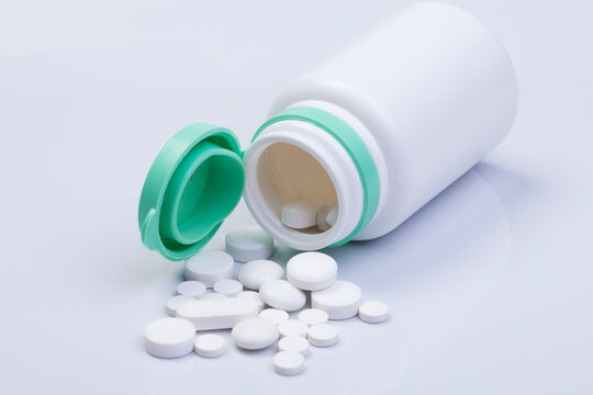 Medication bottle and white pills spilled on white background. Medication and prescription pills flat lay background. Opioid epidemic.