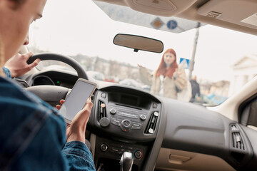 Distracted young male driver looking at the screen of his mobile phone while running over a...