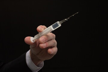 Human hand holding syringe with vaccine on black background