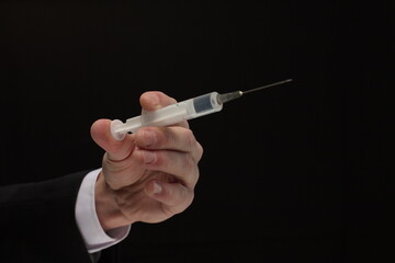 Human hand holding syringe with vaccine on black background