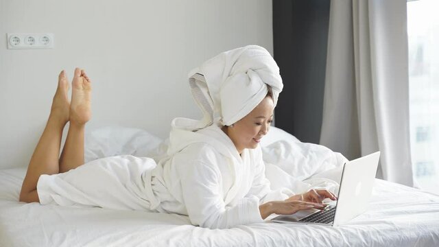 young woman lying in bed working remotely online on a laptop, due to the coronavirus pandemic, many people work remotely at home.