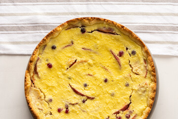 Delicious sweet cheese pie with apples and cranberries, fruit and berry curd pie on a white background with a kitchen towel, top view