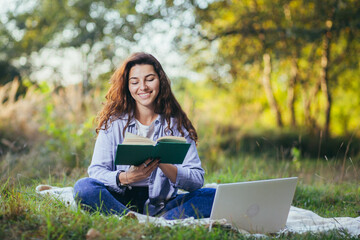 Beautiful woman with curly black hair, resting sitting on a mat in the park on the grass, and uses...