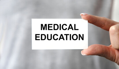 The girl holds a card with the text medical education in front of her.